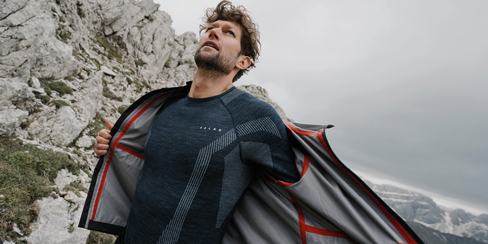 Ein Mann zieht sich gerade die Jacke aus und trägt darunter die Wool-Tech Serie in blau