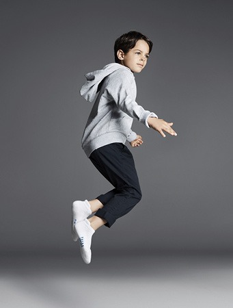 Ein dynamisch springender Junge in grauem Hoodie und dunkler Hose trägt die FALKE Cool Kick Sneakersocken in Weiß für optimalen Tragekomfort.