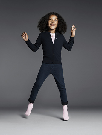 Ein lachendes Mädchen mit lockigen Haaren springt fröhlich in die Luft und trägt die weichen FALKE Family Socken in Rosa.
