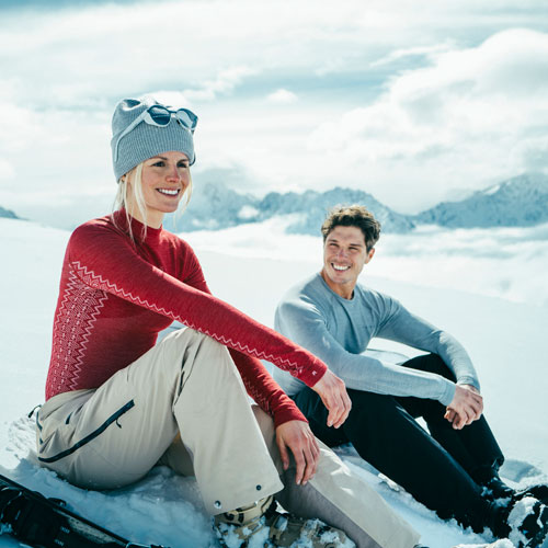 Ein Pärchen sitzt im Schnee und trägt die Funktionsunterwäsche